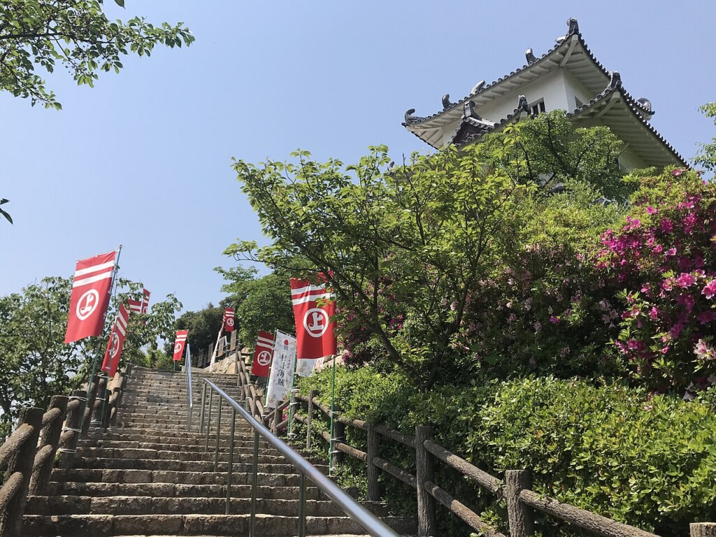 赤い幟が並ぶ石段の参道と、上に建つ城郭風の建物