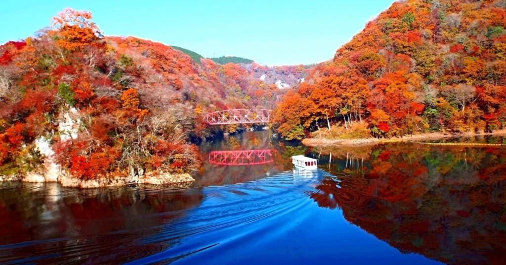 紅葉に染まる神龍湖と赤い鉄橋、湖を進む遊覧船